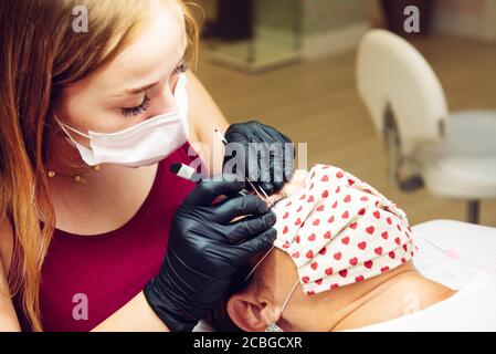 Langhaarige blonde junge Frau auf falsche Wimpern, um Dame im Schönheitssalon mit Masken, neue normale Stockfoto