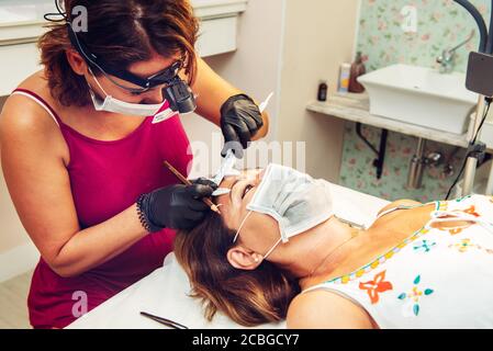Kosmetikerin im Beauty-Center, die Messungen an Kunden für eine Augenbraue Behandlung, mit Masken während der neuen Normalität Stockfoto