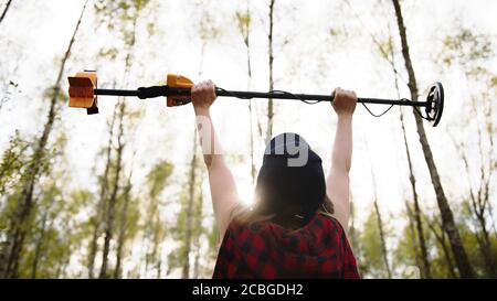 Schatzsucher, junge Frau hält Metalldetektor in der Luft im Wald. Hochwertige Fotos Stockfoto