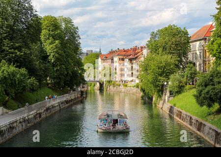 Ljubljana, Slowenien - 16. Juli 2018: Ein Touristenboot, das von der Jakobsbrücke entlang des Flusses Ljublijanica fährt, nachmittags in Ljubljana in su Stockfoto