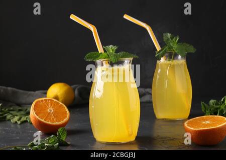 Hausgemachte Limonade aus Zitronen und Orangen, verziert mit Minze in hohen Gläsern mit Röhren auf dunklem Hintergrund, Horizontalformat Stockfoto