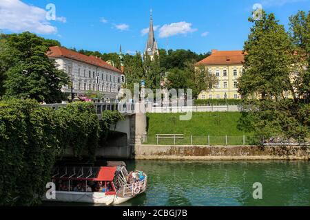 Ljubljana, Slowenien - 16. Juli 2018: Ein Touristenboot unter der Jakobsbrücke auf dem Fluss Ljublijanica, Ljubljana, Slowenien Stockfoto