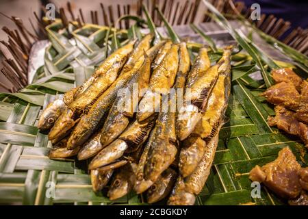 Gegrillter Fisch auf Spieße serviert auf Palmblättern Tisch in der Nähe von oben mit Kopieplatz. Fischspieße auf Palmblättern, traditionelle Mahlzeit Stockfoto
