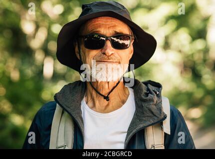 Porträt eines älteren Mannes, der einen Rucksack trägt hut und Brille blicken auf die Kamera Stockfoto