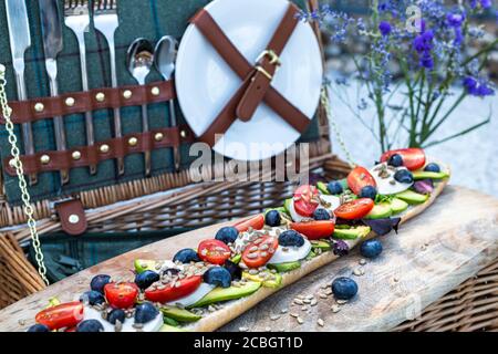 Stilvolles Picknick im Sommer mit Picknickkorb und vegetarischem Baguette mit Avocado, Tomaten und Mozarella-Käse Stockfoto