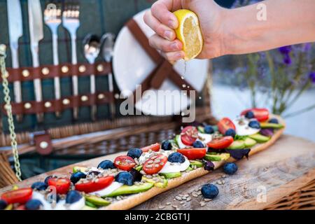 Stilvolles Picknick im Sommer mit Picknickkorb und vegetarischem Baguette mit Avocado, Tomaten und Mozarella-Käse Stockfoto