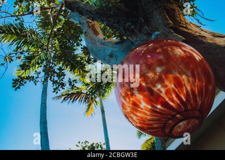 Ein großer runder Baumschmuck, der an einem Palmenbaum hängend ist Stockfoto