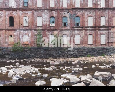 Verlassene Fabrik am Wasserrand. Altes Gebäude auf dem felsigen Fluss. Braune Ziegelmauer. Wasserstrom Stockfoto
