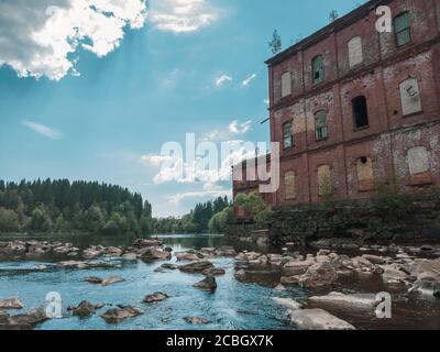 Verlassene Fabrik am Wasserrand. Altes Gebäude auf dem felsigen Fluss. Braune Ziegelmauer. Wasserstrom Stockfoto
