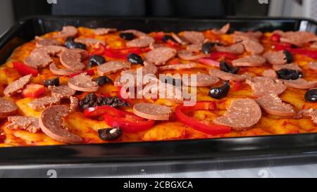 Große Pfanne mit hausgemachter Pizza, ein Mann streut geriebenen Käse auf der Pizza. Stockfoto