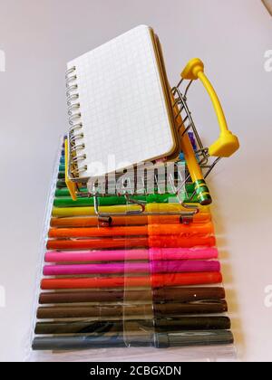 Miniatur-Warenkorb gelb mit Notizblock auf bunten Stiften Stockfoto