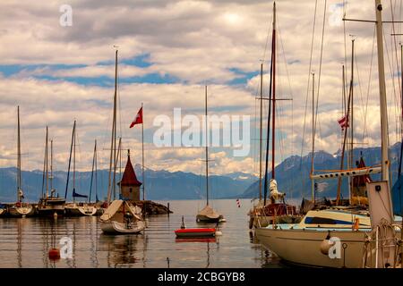 Ein Blick auf die Marina an der Küste des Genfer Sees, Schweiz. Klares Wasser des Sees, ein Vintage-Leuchtturm, Dock, Pier, Segel und ein Schweizer Stockfoto