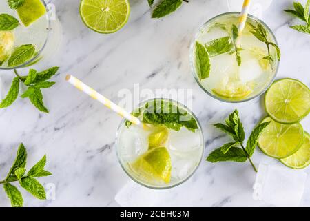 Mojito Cocktail oder Mocktail, traditionelles frisches Getränk mit Limette und Minze. Mit Papierhalmen in den Getränken. Draufsicht, von oben. Auf einem weißen Marmortabl Stockfoto
