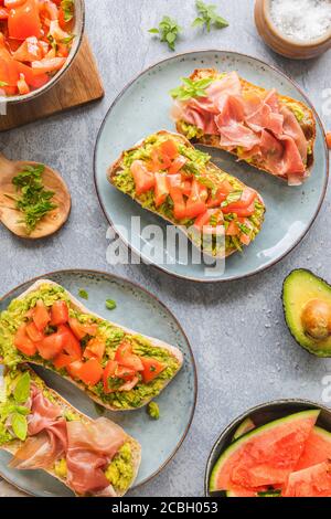 Hausgemachtes Brot mit Avocado-Aufstrich, gehackten Tomaten und Kräutern. Mit Parmaschinken. Gesundes Frühstückskonzept von oben gesehen. Mit Kopierbereich Stockfoto