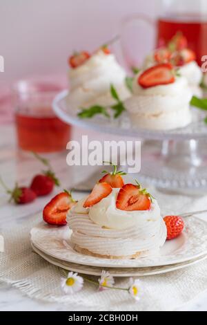 Mini pavlova Baiser Nester mit Schlagsahne und frischen Erdbeeren. Auf dem Tisch stehen Erdbeerlimonade und weitere pavlova-Meringues Stockfoto