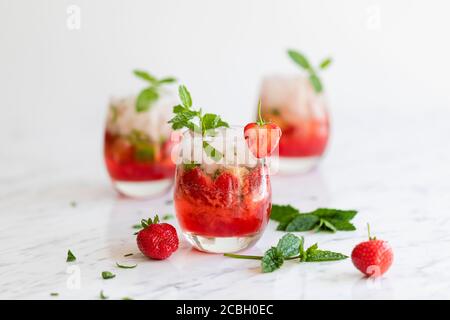 Frische Erdbeer Mojito Getränke. Es gibt drei Getränke auf dem weißen Marmortisch, und sie sind mit Erdbeeren und frischer Minze dekoriert. Es gibt s Stockfoto