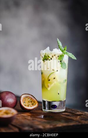 Passionsfrucht Mojito Cocktail und Mocktail in einem hohen Glas, mit zerstoßenem Eis, Limette und Minzblättern. Das Getränk steht auf einem alten Holztisch Stockfoto