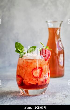 Ein rotes Getränk mit Eis und in Scheiben geschnittenen Erdbeeren, garniert mit Minze und einer frischen Erdbeere., und eine Karaffe der gleichen Flüssigkeit in einem der Hintergrund. Das d Stockfoto