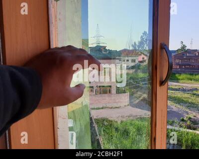 Eine Person mit Schutzmaske, die aus dem Fenster des Hauses schaut. Menschen selbst zu Hause isoliert, durch ihre Fenster Spiegel genommen. Stockfoto