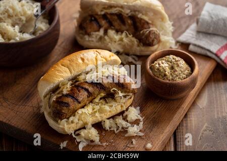 Gegrillte Bratwurst mit Sauerkraut auf einem Brötchen und Senf in Eine Schüssel auf einem Holzbrett Stockfoto