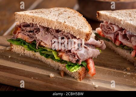 Roastbeef Sandwich mit Salat und Tomaten auf Vollkorn Brot in zwei Hälften geschnitten Stockfoto