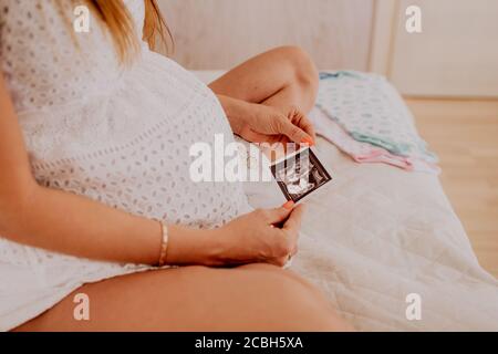 Schwangere Frau, die auf ihre Baby Zwillinge Sonographie. Glückliche werdende Dame genießt das erste Foto von ihren Kindern, Gesicht ist nicht erkennbar. Stockfoto