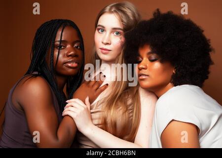 Junge hübsche kaukasische, afro, skandinavische Frau posiert fröhlich zusammen auf braunem Hintergrund, Lifestyle diverse Nationalität Menschen Konzept Stockfoto