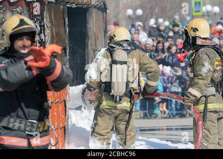 Gruppe von Feuerwehrleuten, die das Feuer aus einem Löschschlauch löschen und dabei Wasser-Schaumstofffass mit luftmechanischem Schaum verwenden Stockfoto