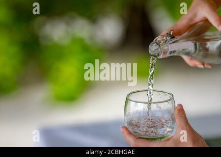 Wasser gießen. Nahaufnahme Gießen gereinigtes frisches Trinkwasser aus der Flasche auf den Tisch auf einem natürlichen unscharfen Hintergrund Stockfoto