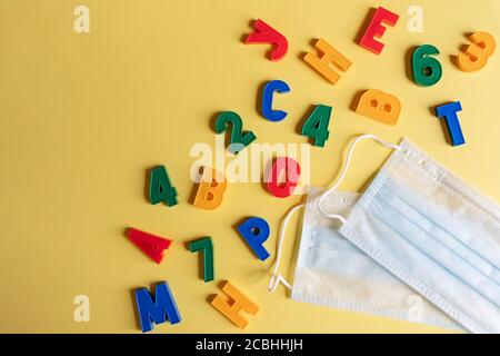 Mehrfarbige englische Buchstaben und Zahlen mit medizinischer Gesichtsmaske auf gelbem Hintergrund. Schutz von Schulkindern vor dem Virus, Coronavirus, covid Stockfoto
