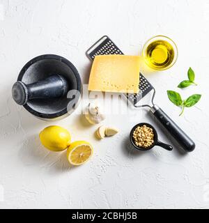 Quadratisches grünes Basilikum Pesto alla Genovese italienische Rezepturzutaten auf weißer Tafel von der Seitenansicht. Parmesankäse, Basilikumblätter, Pinienkerne, Oliven Stockfoto