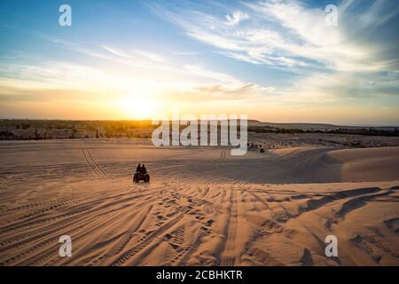 Sonnenaufgang in der Wüste. Szene mit zwei ATV-Biker. Touristen fahren auf einem Geländewagen durch die Sanddünen der vietnamesischen Wüste. Safari früh in der Stockfoto