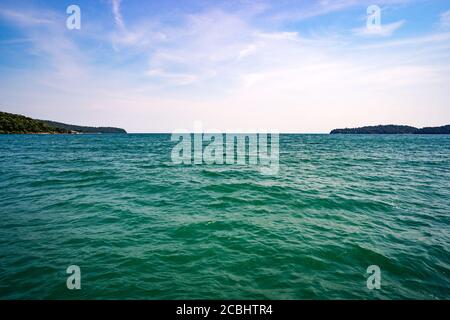 Türkisfarbenes Wasser im Südchinesischen Meer. Die Horizontlinie zwischen Meer und blauem Himmel mit Wolken. Kleine Inseln im Hintergrund. Stockfoto