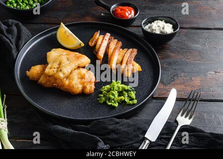 Fish & Chips mit Dip und Zitrone schwarzen Teller mit Britische traditionelle Küche mit Bier-zerschlagene Kabeljau und Pommes frites und Eine Seite der Tartarsauce matschig Stockfoto