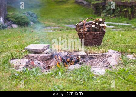 Lagerfeuer im Garten, neben einem Korb mit Brennholz Stockfoto