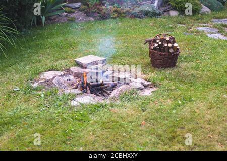 Lagerfeuer im Garten, neben einem Korb mit Brennholz Stockfoto