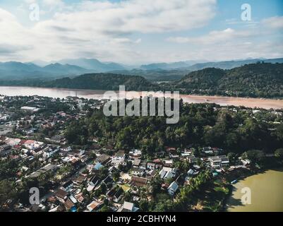 Luang Prabang, Laos. Luftaufnahme der Stadt Luang Prabang in Laos. Wolkiger Himmel über einer kleinen Stadt, umgeben von Bergen. Autoverkehr und Fluss Stockfoto