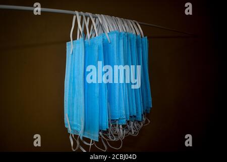 Ein Bündel von blauen Gesichtsmasken werden an einem Tuch Stange zum Trocknen Zweck nach der Reinigung sie für die Wiederverwendung aufgehängt. Wiederverwendbare Masken mit aufgehängten Clips Stockfoto