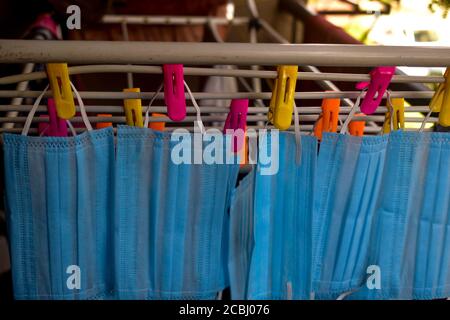 Ein Bündel von blauen Gesichtsmasken werden an einem Tuch Stange zum Trocknen Zweck nach der Reinigung sie für die Wiederverwendung aufgehängt. Wiederverwendbare Masken mit aufgehängten Clips Stockfoto