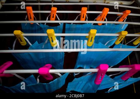 Ein Bündel von blauen Gesichtsmasken werden an einem Tuch Stange zum Trocknen Zweck nach der Reinigung sie für die Wiederverwendung aufgehängt. Wiederverwendbare Masken mit aufgehängten Clips Stockfoto