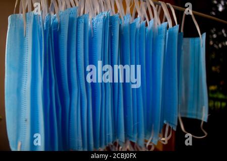 Ein Bündel von blauen Gesichtsmasken werden an einem Tuch Stange zum Trocknen Zweck nach der Reinigung sie für die Wiederverwendung aufgehängt. Wiederverwendbare Masken mit aufgehängten Clips Stockfoto