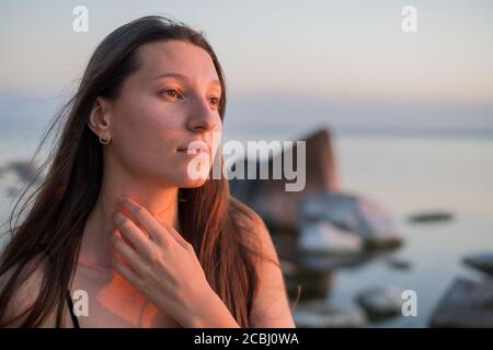 Junge Frau, die den Hals in der Nähe des Meeres berührt Stockfoto