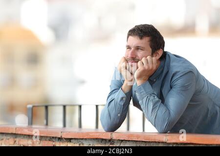 Nachdenklicher Mann, der auf einem Balkon auf einem nachdenklichen Stadt Stockfoto