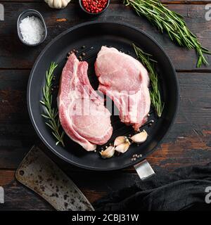 Rohes Schweinesteak auf dem Knochen in Bratpfanne Mit Metzgermesser oder Spaltmesser und Einlagen für Grillplatte Blick quadratisch auf vintage dunklen Holztisch Stockfoto