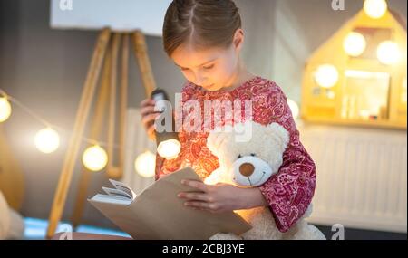 Nettes kleines Mädchen Buch mit Taschenlampe in beleuchteten Raum zu lesen Stockfoto