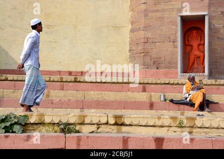 Varanasi Ganga Ghat EIN Hindu-heiliger sitzt vor dem Hanuman-Tempel und ein muslimischer Junge geht durch das Ghat. Stockfoto