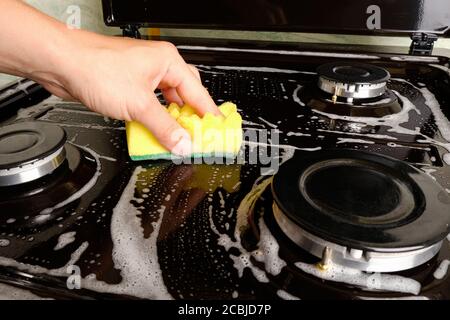 Frau reinigt Gasherd mit einem Waschlappen und Schaum, Oberflächenreinigung, Reinigung der Küche, Küchengeräte. Stockfoto