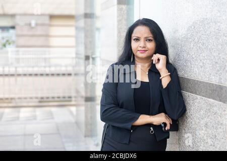 Eine indische Frau, die mit gekreuzten Armen in einem städtischen Unternehmensbereich steht. Stockfoto