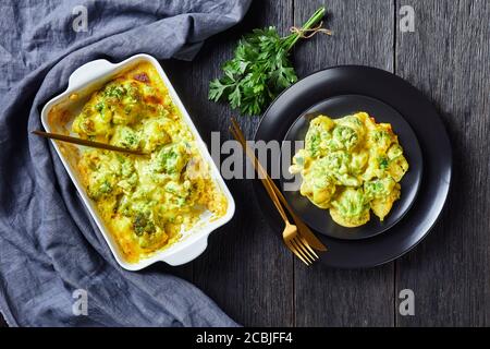 Kitschiger Broccoli-Backen, Broccoli-Auflauf auf schwarzem Teller und in einer Auflaufform auf dunklem Holztisch, horizontale Ansicht von oben, flaches Lay, freier Spac Stockfoto