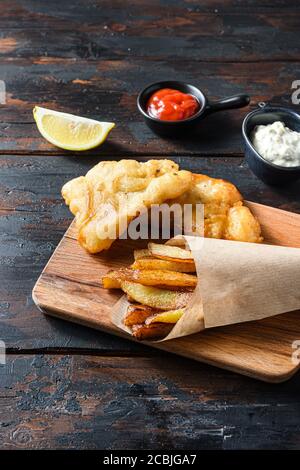 Britische traditionelle Fisch und Chips mit pürierten Erbsen, Tartarsauce Inn zerknitterten Papierkegel auf Holz Schneidebrett Dip und Zitrone - gebratenen Kabeljau, französisch Stockfoto